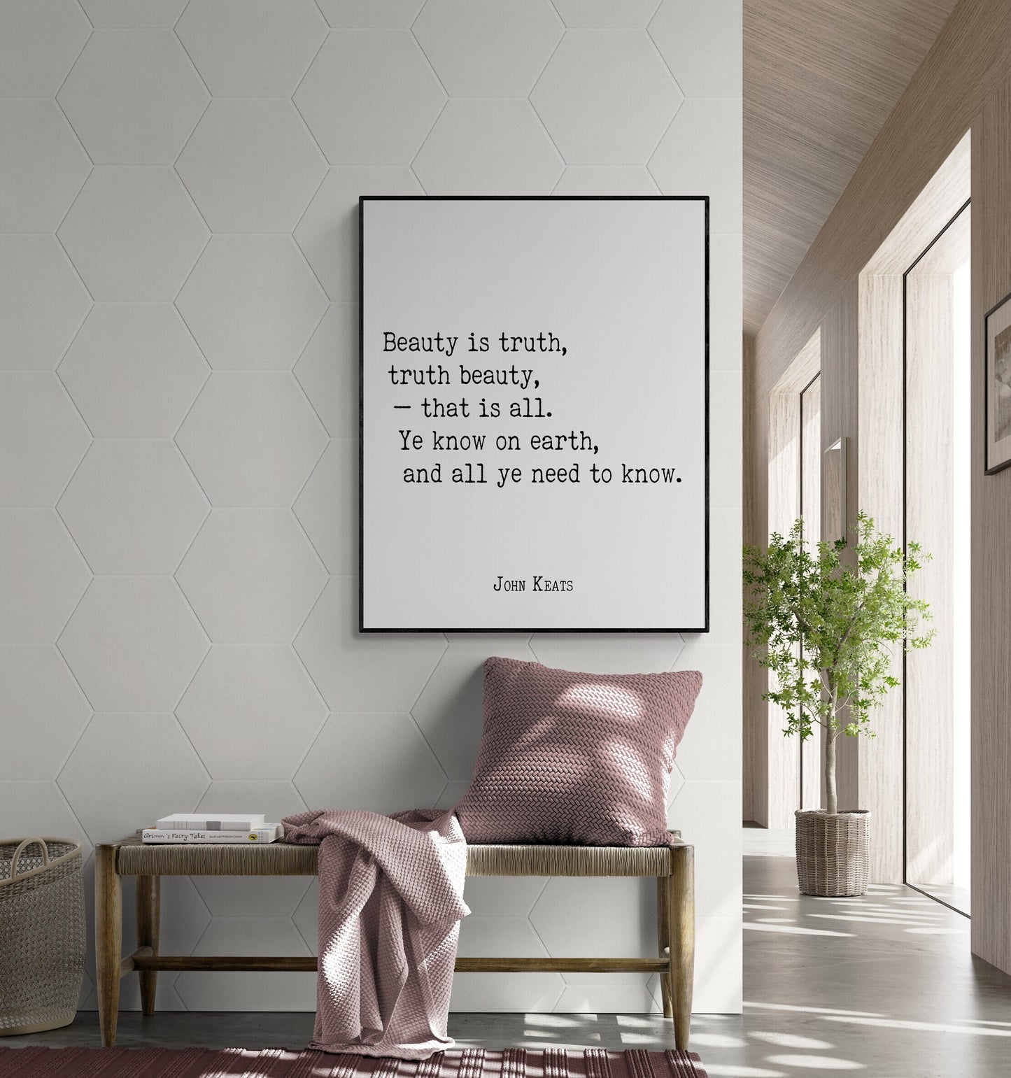 May include: A black framed print with a white background and black text that reads 'Beauty is truth, truth beauty, - that is all. Ye know on earth, and all ye need to know. JOHN KEATS' The print is hanging on a white wall with a hexagonal pattern. A pink throw blanket is draped over a wooden bench with a pink pillow. A green plant is in a brown pot on the floor next to a window.