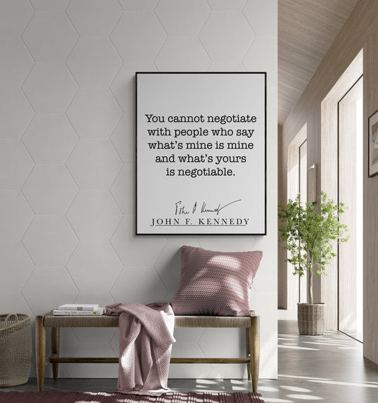 May include: A black framed quote on a white wall with a black signature below the text. The quote reads &#39;You cannot negotiate with people who say what&#39;s mine is mine and what&#39;s yours is negotiable.&#39; The signature reads &#39;John F. Kennedy&#39;. The quote is hanging above a light brown bench with a pink throw blanket and a pink pillow. A green plant is in a brown pot on the right side of the image.