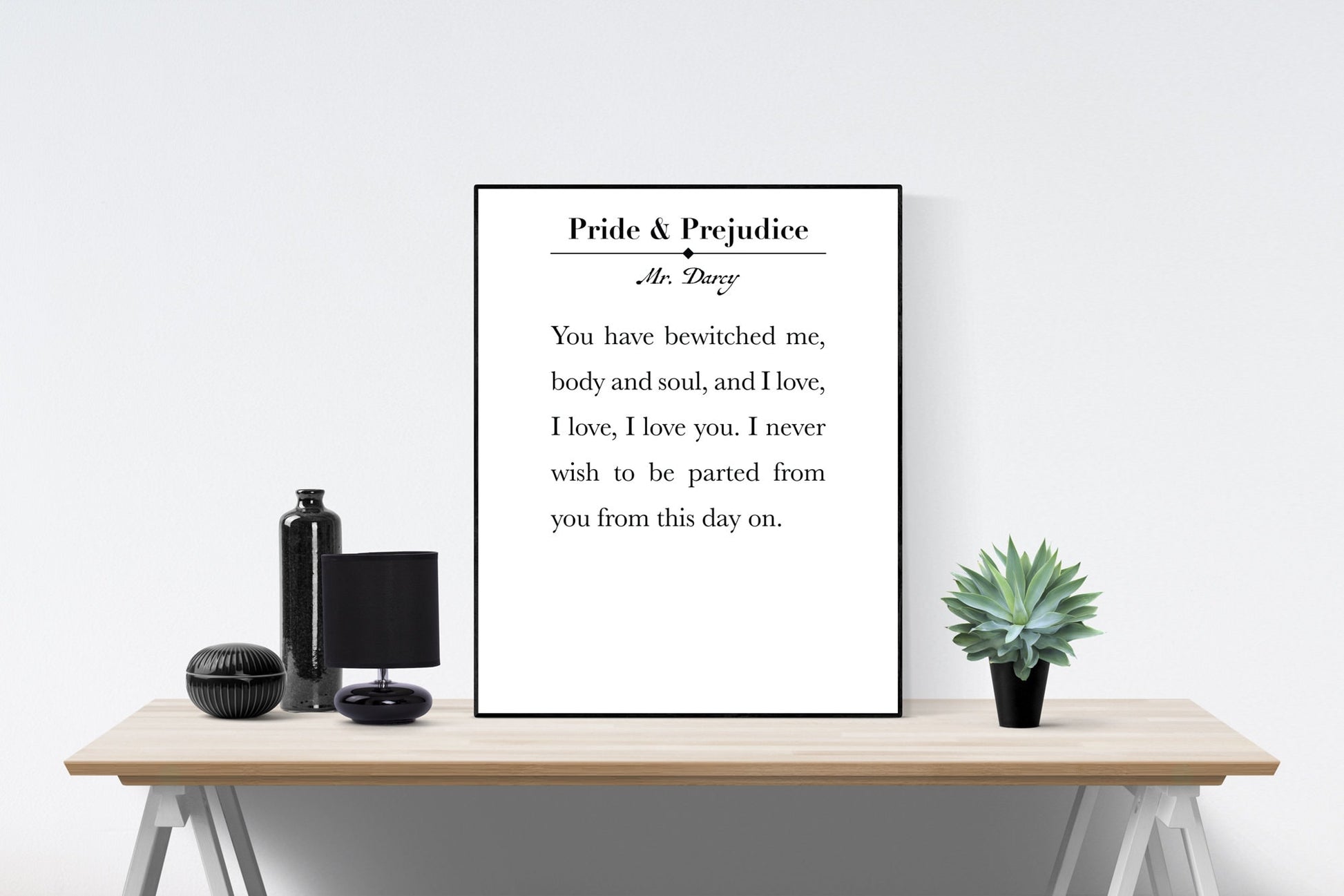 May include: A black and white framed print with the text &#39;Pride & Prejudice&#39; and &#39;Mr. Darcy&#39; above a quote that reads &#39;You have bewitched me, body and soul, and I love, I love, I love you. I never wish to be parted from you from this day on.&#39; The print is sitting on a wooden table with a black vase, a black lamp, and a small green plant.