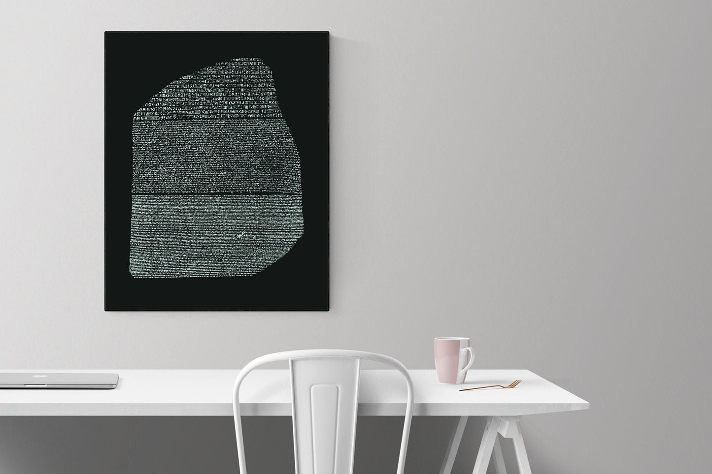 May include: A black and white image of the Rosetta Stone on a black background. The image is framed and hanging on a white wall above a white desk with a white chair and a pink mug on the desk.