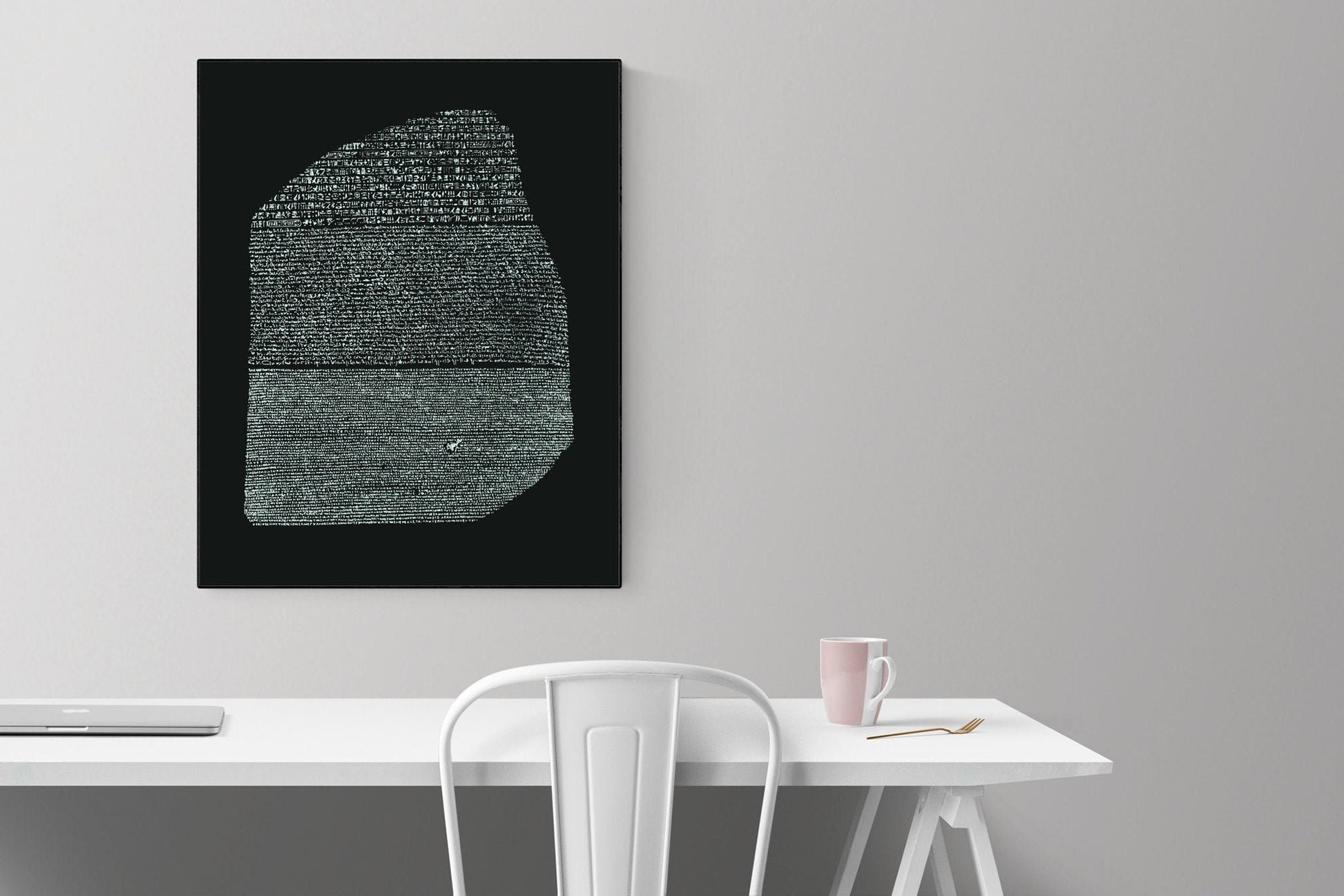 May include: A black and white image of the Rosetta Stone on a black background. The image is framed and hanging on a white wall above a white desk with a white chair and a pink mug on the desk.