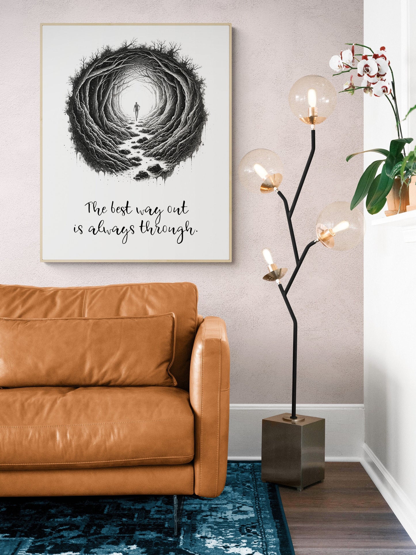 May include: A black and white illustration of a person walking through a tunnel of trees. The text below the illustration reads &#39;The best way out is always through.&#39; The illustration is framed and hanging on a white wall. A brown leather sofa sits in front of the illustration. A black floor lamp with gold globe lights sits to the right of the sofa. A blue rug sits in front of the sofa.