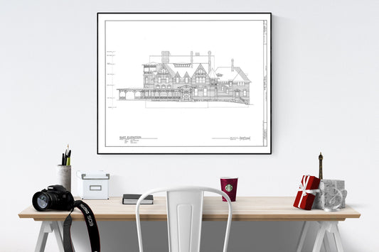 May include: A black and white architectural drawing of a house with a large porch. The drawing is framed and hanging on a white wall above a desk. The drawing is titled &#39;East Elevation&#39;.