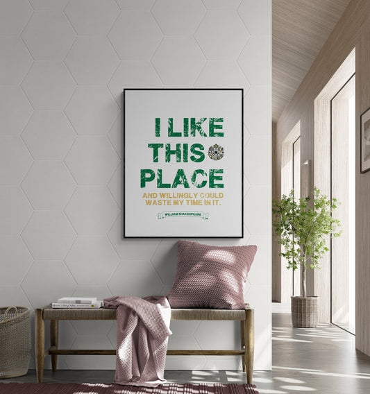 May include: A black framed poster with white background and green text that reads &#39;I LIKE THIS PLACE AND WILLINGLY COULD WASTE MY TIME IN IT. WILLIAM SHAKESPEARE&#39; The poster is hanging on a white wall with a hexagonal pattern. A wooden bench with a pink throw blanket and a pink pillow is in front of the poster.