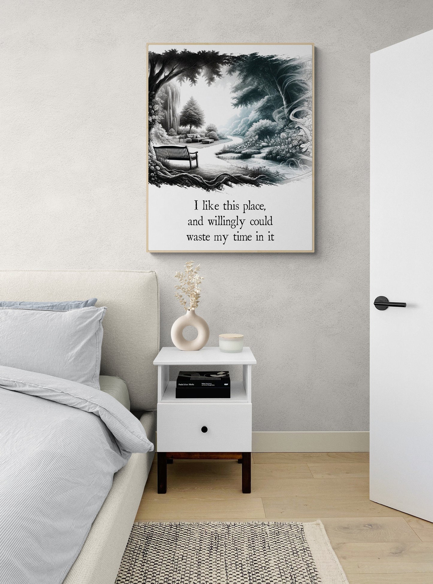 May include: A white nightstand with a drawer and a shelf. The nightstand has a black knob on the drawer and is sitting on a light brown wood floor. A book is on the shelf. A white vase with dried flowers is on the top shelf. A framed black and white drawing of a park scene with a bench and a path is hanging on the wall behind the nightstand. The drawing has text that reads: 'I like this place, and willingly could waste my time in it.'