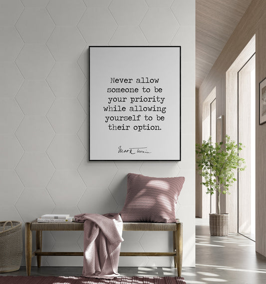May include: A black framed print with a white background and black text that reads 'Never allow someone to be your priority while allowing yourself to be their option. Mark Twain.' The print is hanging on a white hexagonal tile wall. A wooden bench with a pink throw blanket and pillow is in front of the print. A potted plant is on the right side of the image.