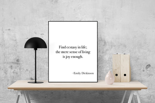 May include: A black and white printable quote poster with the text 'Find ecstasy in life; the mere sense of living is joy enough. -Emily Dickinson' displayed on a white background. The poster is framed with a black frame and is sitting on a light brown wooden table.