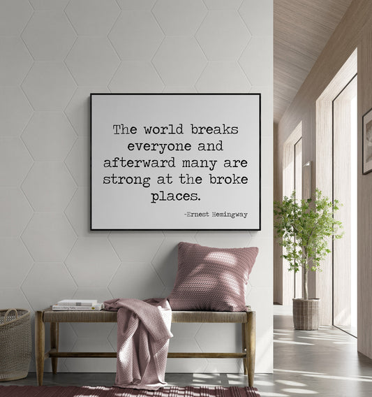 May include: A black and white typography print with the quote 'The world breaks everyone and afterward many are strong at the broke places.' -Ernest Hemingway. The print is hanging on a white wall with a hexagonal pattern. A wooden bench with a pink throw blanket and pillow is in front of the print.