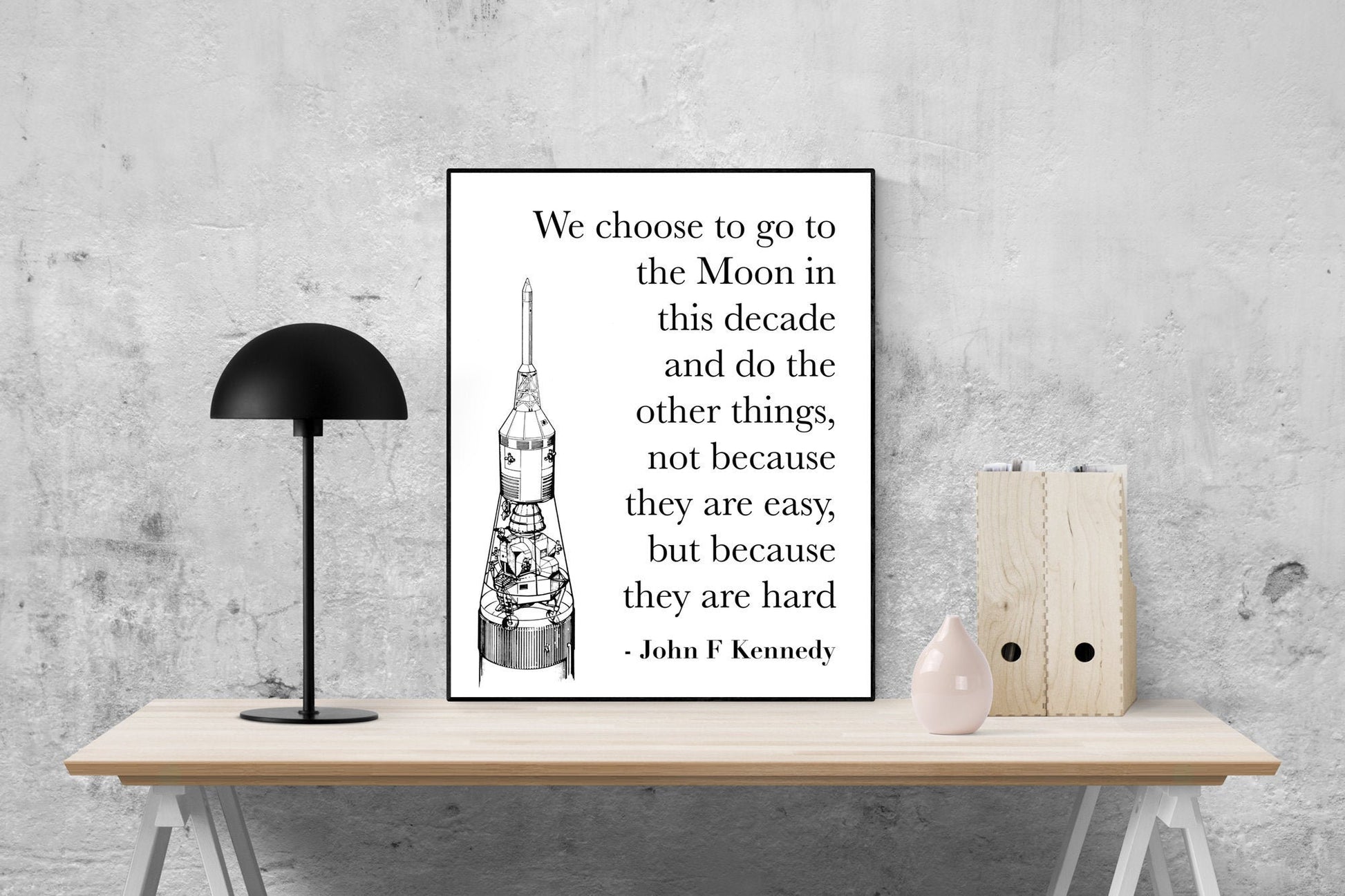 May include: A black and white illustration of a rocket ship with a quote by John F. Kennedy that reads: 'We choose to go to the Moon in this decade and do the other things, not because they are easy, but because they are hard - John F Kennedy'.
