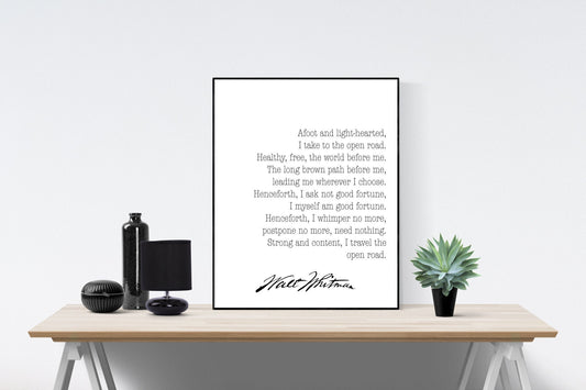 May include: A black framed print with a white background and black text. The text is a poem by Walt Whitman that reads 'Afoot and light-hearted, I take to the open road. Healthy, free, the world before me. The long brown path before me, leading me wherever I choose. Henceforth, I ask not good fortune, I myself am good fortune. Henceforth, I whimper no more, postpone no more, need nothing. Strong and content, I travel the open road.' The poem is signed 'Walt Whitman'.