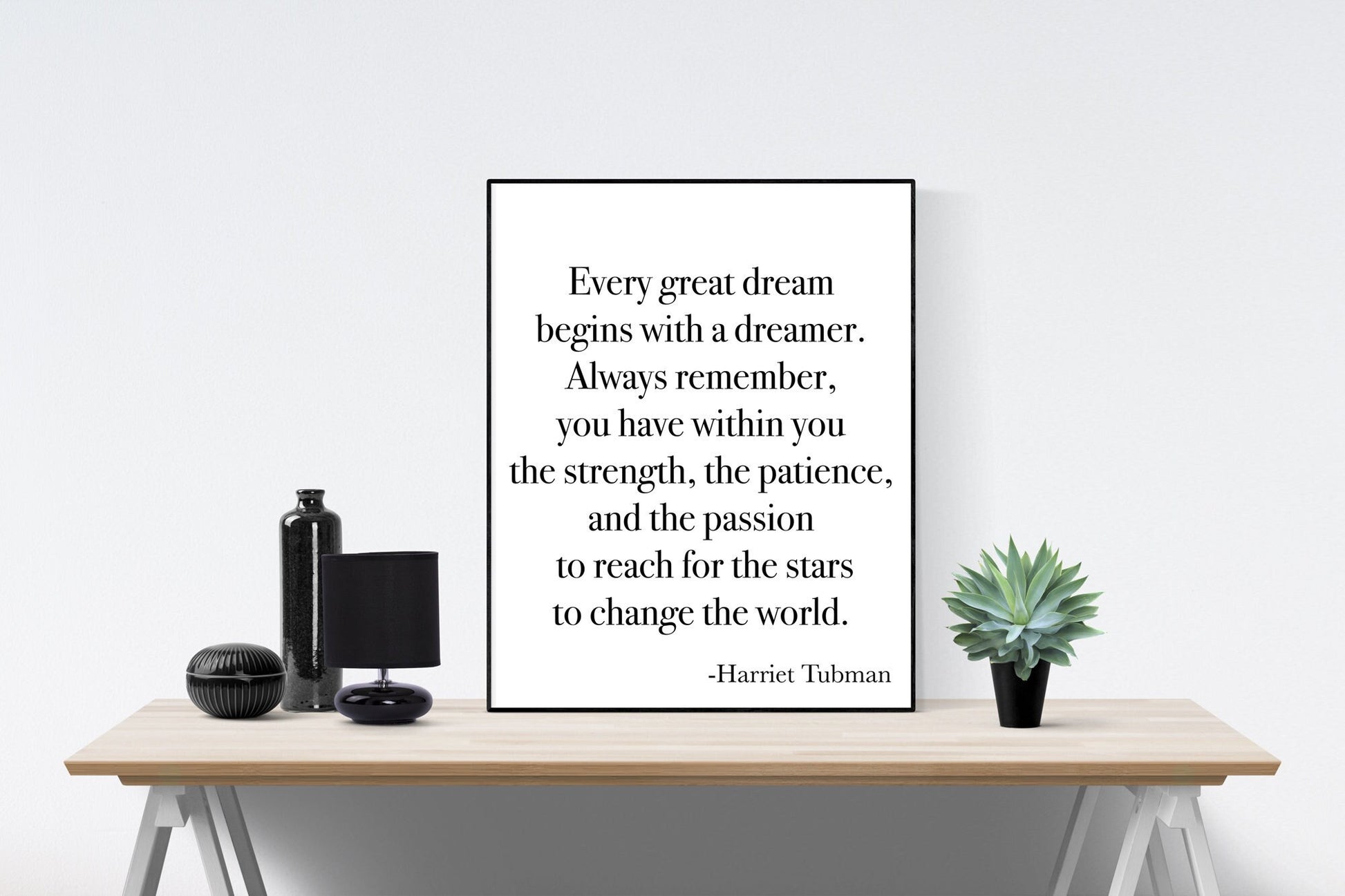 May include: A black and white inspirational quote on a white background. The quote reads: 'Every great dream begins with a dreamer. Always remember, you have within you the strength, the patience, and the passion to reach for the stars to change the world.' -Harriet Tubman. The quote is framed and displayed on a wooden table with a black vase, a black lamp, and a potted succulent plant.