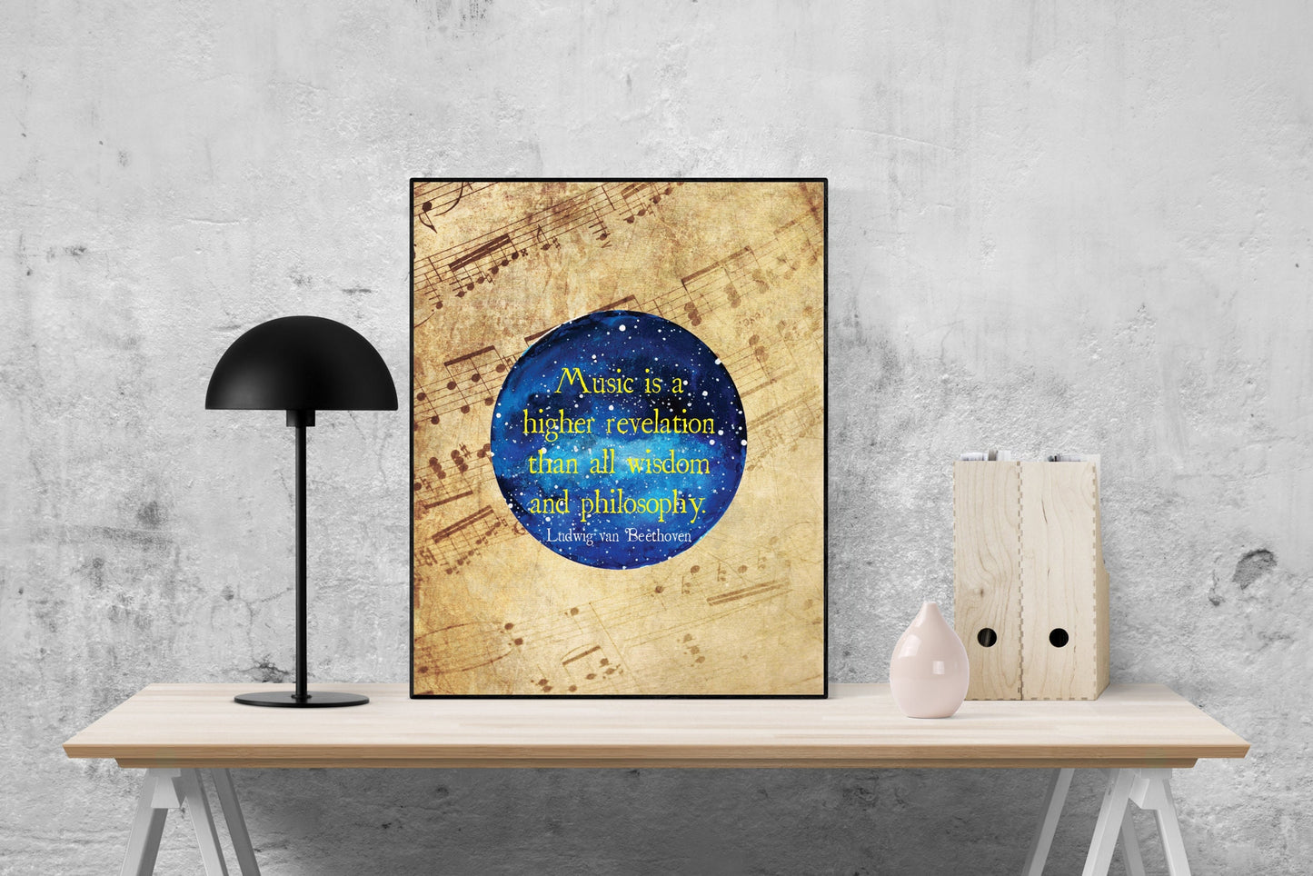 May include: A framed print with a blue and white watercolor galaxy background. The print features a quote in yellow text that reads 'Music is a higher revelation than all wisdom and philosophy. Ludwig van Beethoven.' The print is displayed on a wooden table with a black lamp and a white vase.