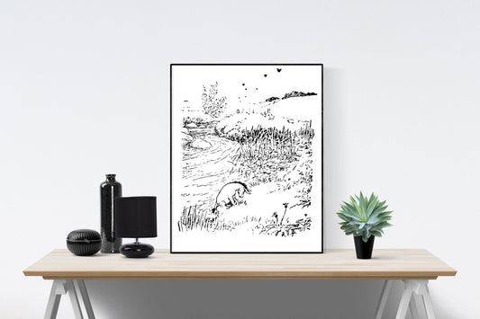 May include: A black and white line drawing of a river scene with two animals, one in the water and one on the bank. The drawing is framed and displayed on a wooden table with a black bottle, a black lamp, and a green succulent plant.