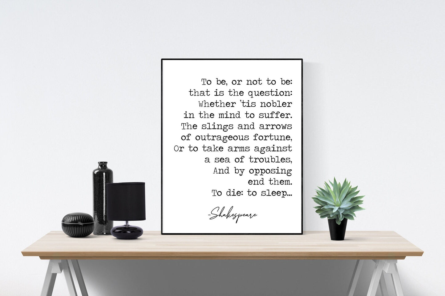 May include: A black and white framed print of a Shakespeare quote on a wooden table. The quote reads: 'To be, or not to be: that is the question: Whether 'tis nobler in the mind to suffer. The slings and arrows of outrageous fortune, Or to take arms against a sea of troubles, And by opposing end them. To die: to sleep... Shakespeare'.