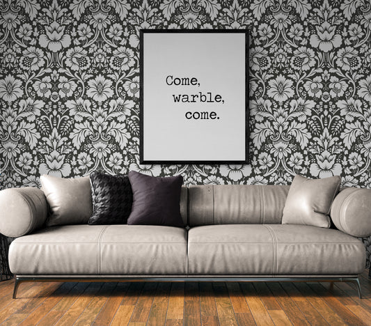 May include: A gray couch with black pillows in front of a black and white floral wallpaper. A black framed picture with the text 'Come, warble, come.' is hanging on the wall above the couch.